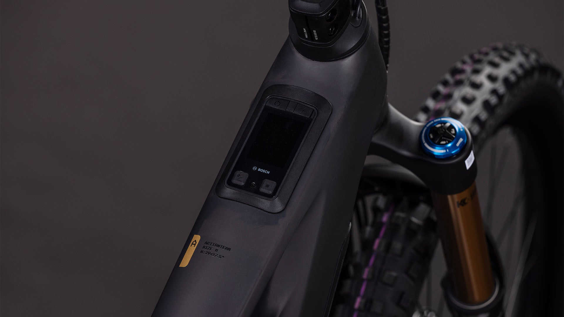 Nahaufnahme des CUBE Stereo Hybrid ONE77 HPC AT 800 carbon'n'gold 2026 E-MTB-Rahmens mit einem im Oberrohr integrierten Bosch-Bedienfeld und einer Federgabel mit blauem Einstellknopf.