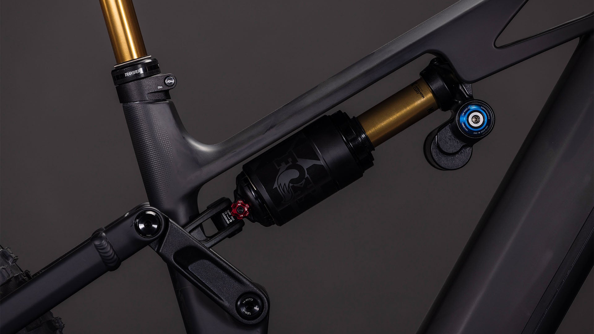 Nahaufnahme des CUBE Stereo Hybrid ONE77 HPC AT 800 carbon'n'gold 2026 mit seinem mattgrauen Carbon-Rahmen, dem hinteren Federbein, der Anlenkung und den goldenen und schwarzen Komponenten, die für Big-Mountain-Fahrten entwickelt wurden.