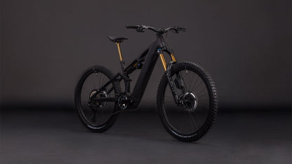 Das CUBE Stereo Hybrid ONE77 HPC AT 800 carbon'n'gold 2026 ist ein modernes schwarzes Elektro-Mountainbike mit Bosch CX-Motor, dicken Reifen, Federung vorne und hinten und goldfarbenen Gabeln, das vor einem schlichten dunklen Hintergrund gezeigt wird.