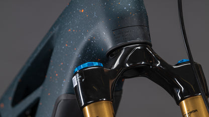Nahaufnahme des CUBE Stereo Hybrid ONE77 HPC SLT 800 E-Bike in galaxy'n'orange (2026), mit goldener und blauer Federgabel und leistungsstarkem Bosch CX-R Motor, vor einem schlichten grauen Hintergrund.
