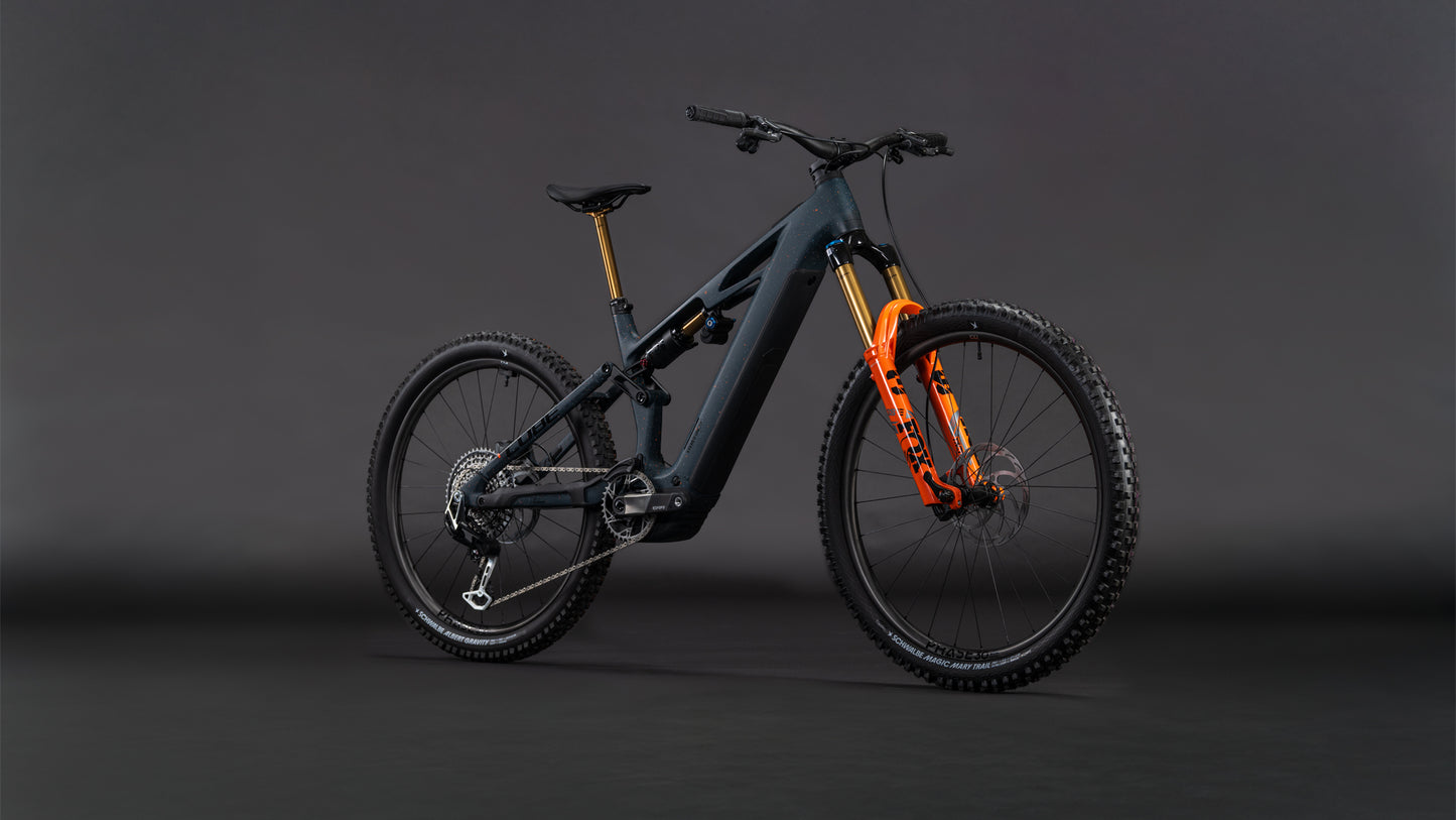 Das CUBE Stereo Hybrid ONE77 HPC SLT 800 galaxy'n'orange 2026 E-Mountainbike mit markantem Rahmen und orangefarbenen Akzenten steht für Big-Mountain-Performance vor dramatischer Kulisse.