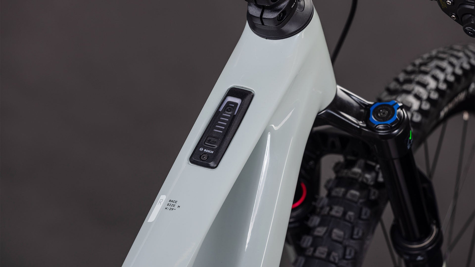 Nahaufnahme des CUBE AMS Hybrid ONE44 C:62 Race 400X reedbeige'n'black 2026 Rahmens von CUBE, die das Bosch-Bedienfeld und die Batterieanzeige auf dem Oberrohr mit einem Bosch SX Motor zeigt. Die vordere Federgabel und der Reifen sind im Hintergrund zu sehen.