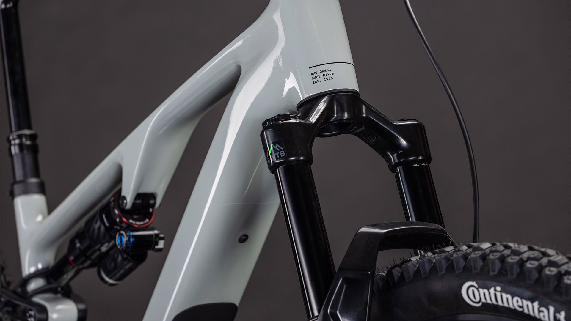 Nahaufnahme eines CUBE AMS Hybrid ONE44 C:62 Race 400X reedbeige'n'black 2026 Mountainbike-Rahmens mit Bosch SX Motor, Federgabel, C:62 Carbonrahmen und Continental-Vorderreifen vor dunklem Hintergrund.