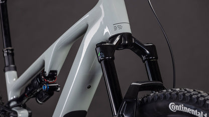 Nahaufnahme eines CUBE AMS Hybrid ONE44 C:62 Race 400X reedbeige'n'black 2026 Mountainbike-Rahmens mit Bosch SX Motor, Federgabel, C:62 Carbonrahmen und Continental-Vorderreifen vor dunklem Hintergrund.