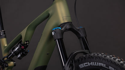 Nahaufnahme des CUBE AMS Hybrid ONE44 C:68X TM 400X reedgreen'n'matrix (2026) Rahmens, die das mattgrüne Finish, die Federgabel, den Stoßdämpfer und den Schwalbe-Reifen vor einem dunklen Hintergrund zeigt.