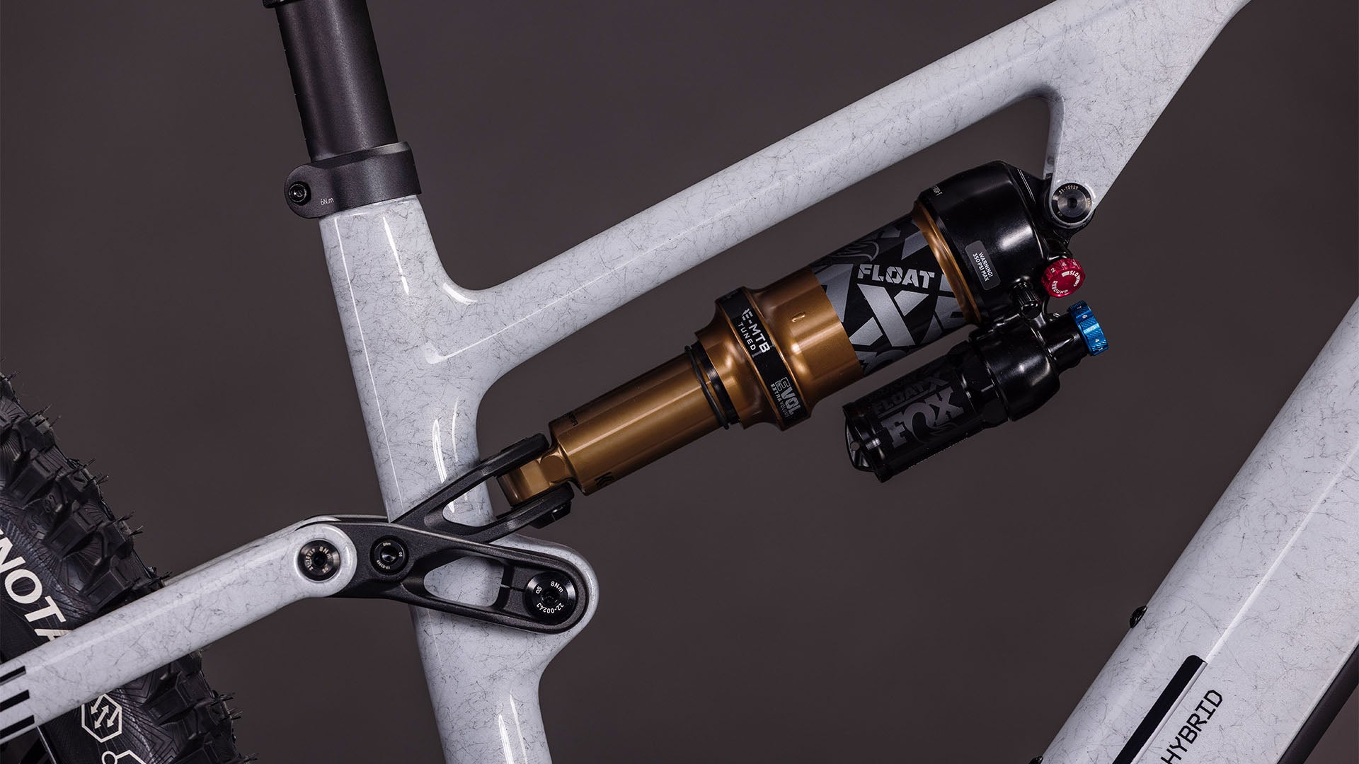 Nahaufnahme der Hinterradaufhängung des CUBE AMS Hybrid ONE44 C:68X SUPER TM 400X. Hervorzuheben sind der FOX Float X-Dämpfer am weißen Carbonrahmen, die sichtbaren Einstellknöpfe und ein Teil des Hinterrads.
