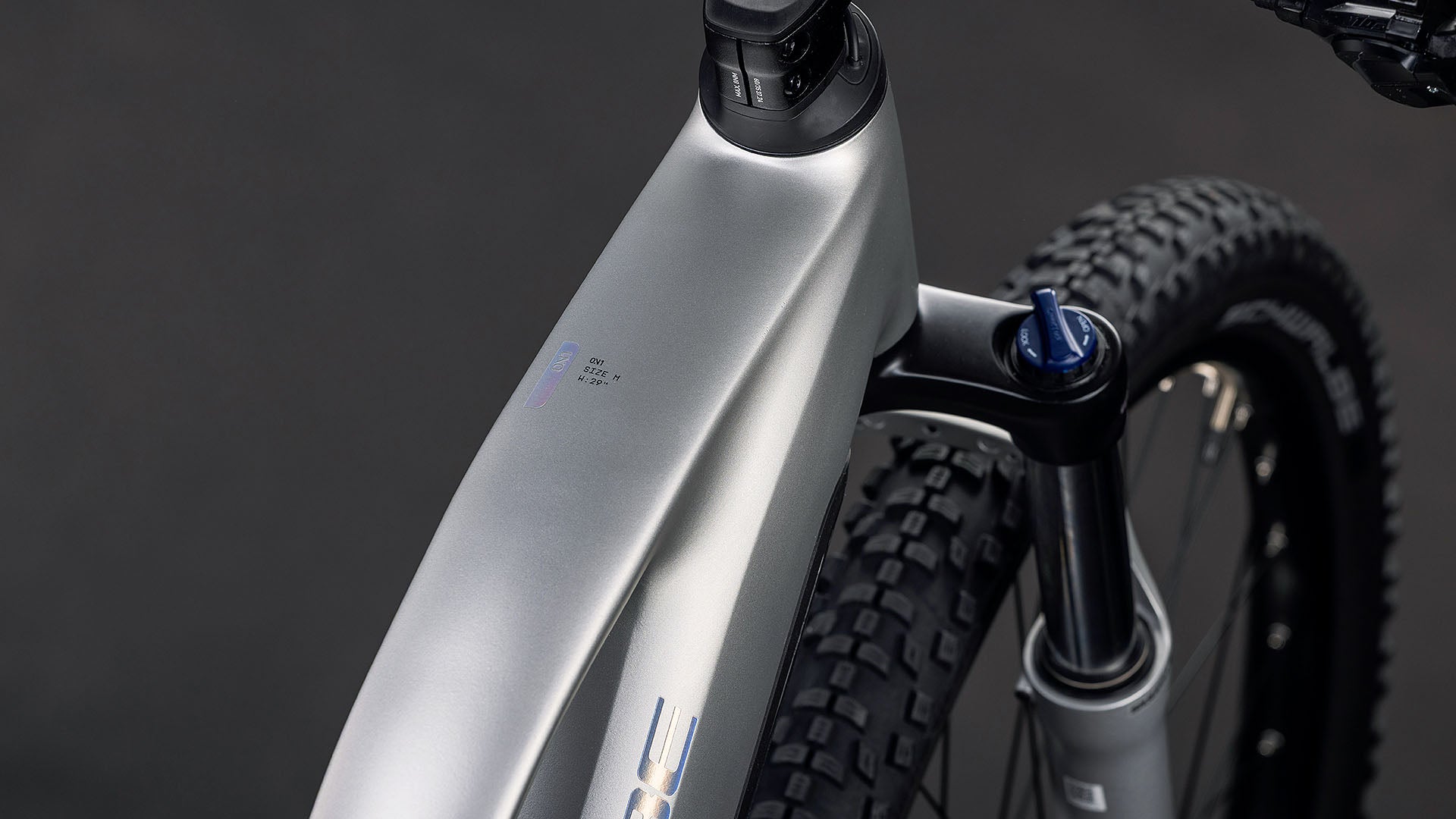 Nahaufnahme des CUBE Reaction Hybrid ONE 800 sleekgrey'n'prism Trapeze 2026 Rahmens, die das Oberrohr, den Bosch Motor, die Federgabel und den Vorderreifen vor einem dunklen Hintergrund zeigt.