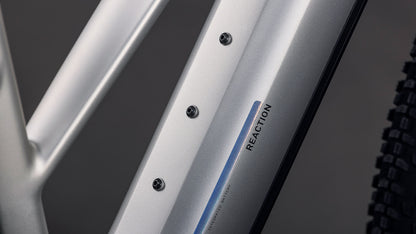 Nahaufnahme eines CUBE Reaction Hybrid ONE 800 sleeky'n'prism Trapeze 2026 Rahmens mit "REACTION"-Schriftzug, drei Befestigungsschrauben und einem Teil eines schwarzen Reifens - ausgestattet mit einem 800-Wh-Akku und Bosch-Motor-System-Kompatibilität.