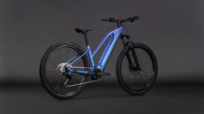 Das CUBE Reaction Hybrid ONE 800 blueiris'n'reflect Trapeze 2026 verfügt über einen metallisch blauen Rahmen, dicke Offroad-Reifen, einen Bosch-Motor, einen 800-Wh-Akku, eine Federgabel, Scheibenbremsen und einen aufrechten Sitz auf einem dunklen, neutralen Hintergrund.