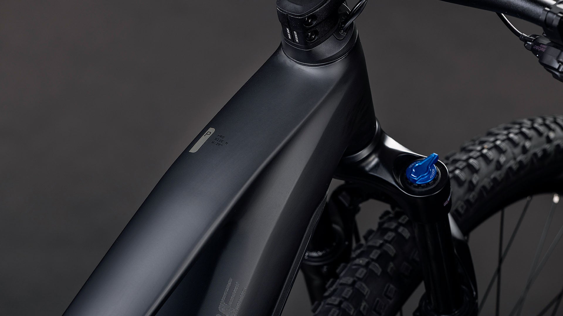 Nahaufnahme des CUBE Reaction Hybrid Pro 800 blackline 2026 E-Mountainbike-Rahmens mit mattschwarzem Finish, auffälliger Bosch CX Antrieb-Integration, sichtbarer Vorderradfederung, detailliertem Reifenprofil und blauem Einstellknopf in der Nähe des Lenkers.