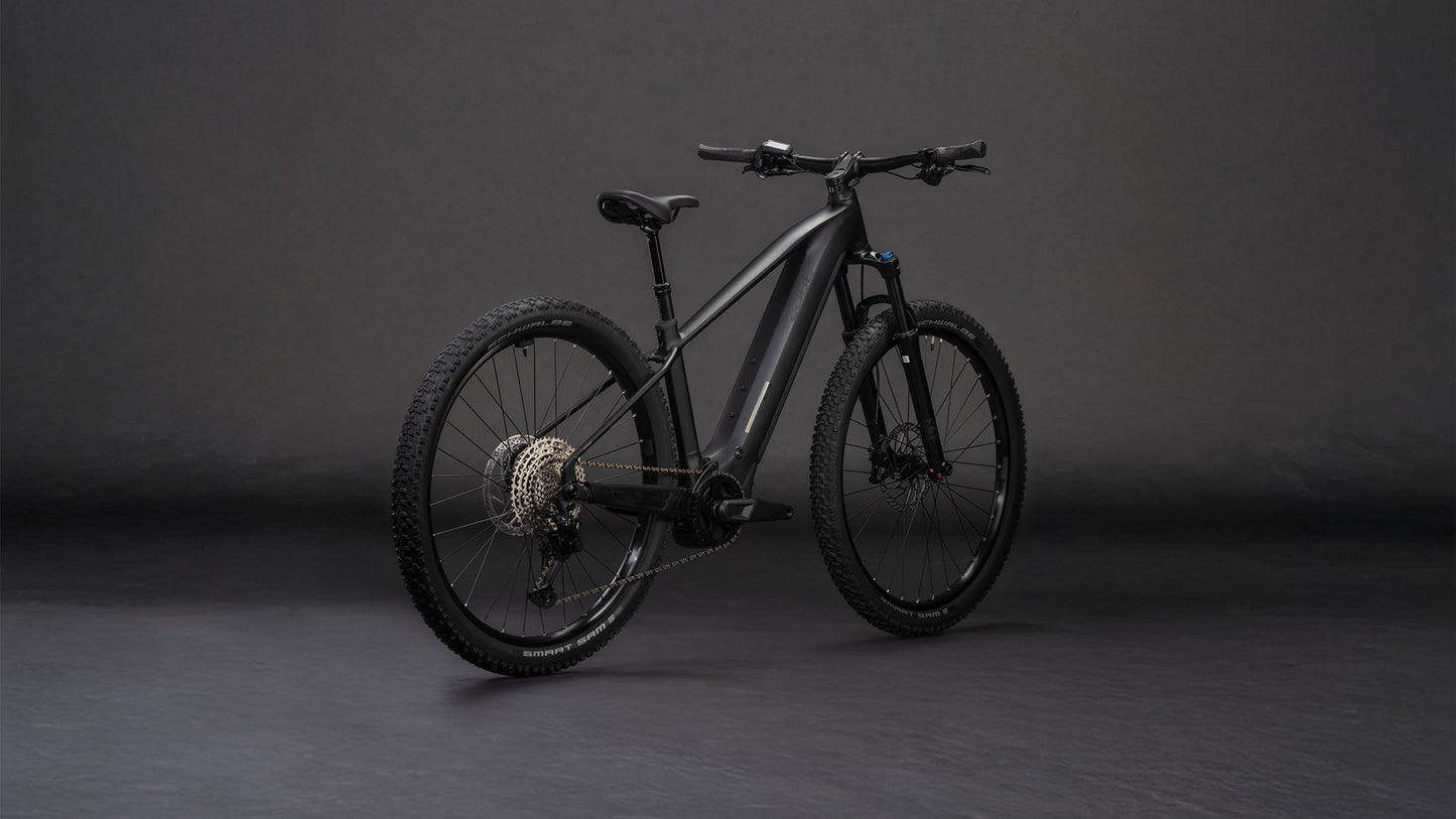 Das E-Mountainbike CUBE Reaction Hybrid Pro 800 blackline 2026 mit Bosch CX-Antrieb und 800-Wh-Akku besticht durch dicke Reifen, einen stabilen Rahmen und eine sichtbare Schaltung, die sich in der hinteren Dreiviertelansicht vor einem dunklen, nahtlosen Hintergrund abzeichnet.