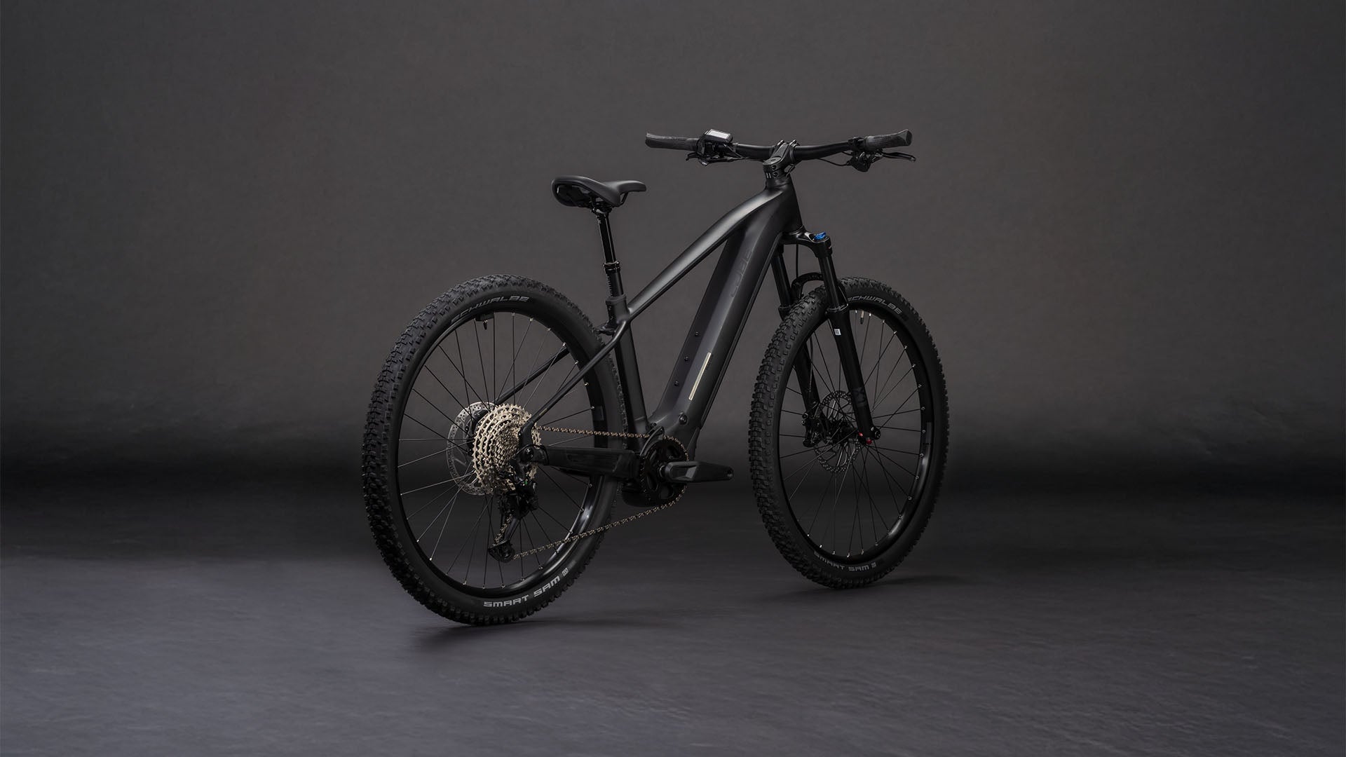 Das E-Mountainbike CUBE Reaction Hybrid Pro 800 blackline 2026 mit Bosch CX-Antrieb und 800-Wh-Akku besticht durch dicke Reifen, einen stabilen Rahmen und eine sichtbare Schaltung, die sich in der hinteren Dreiviertelansicht vor einem dunklen, nahtlosen Hintergrund abzeichnet.