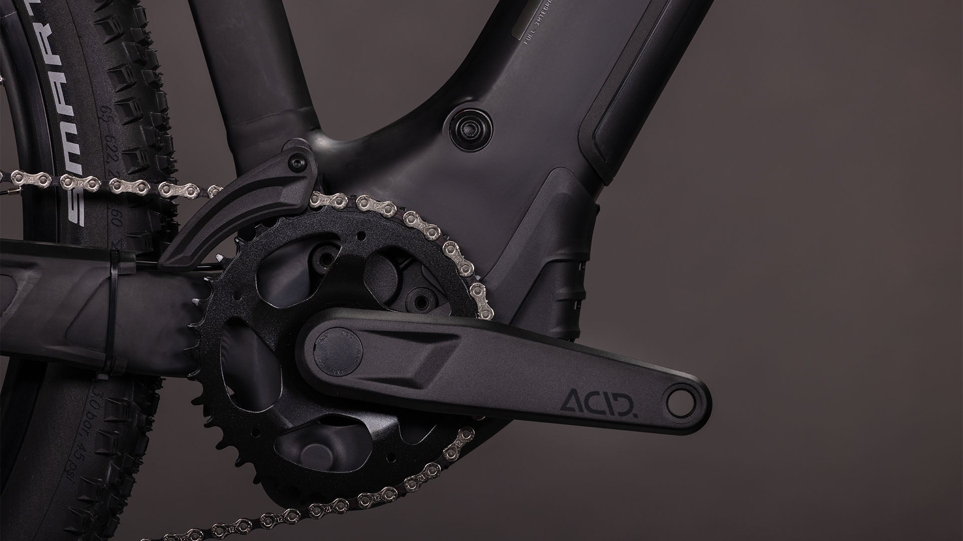 Nahaufnahme der CUBE Reaction Hybrid Pro 800 blackline Trapeze 2026 Kurbelgarnitur, des Kettenblatts und des ACID-Pedalarms. Hervorzuheben sind die Details des Bosch CX-Antriebssystems und des Antriebsstrangs, wobei ein Teil des Hinterrads sichtbar ist.