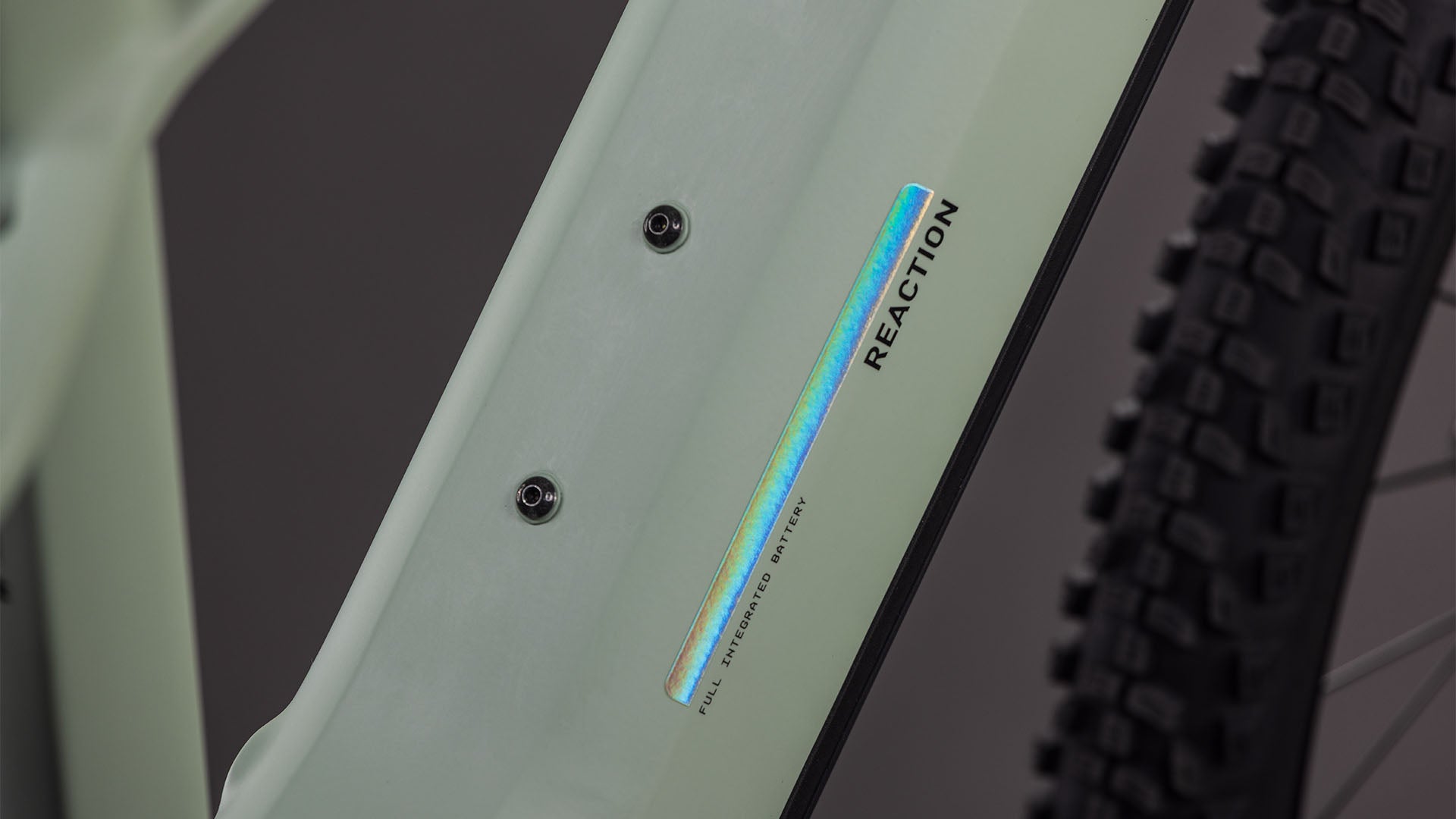 Nahaufnahme des CUBE Reaction Hybrid Pro 800 desertstone'n'driedherbs 2026-Rahmens mit "REACTION"- und irisierendem "FULL INTEGRATED BATTERY"-Schriftzug, zwei Schraubenbefestigungen, einem Teil eines groben Reifens und Bosch CX-Antriebsdetails.