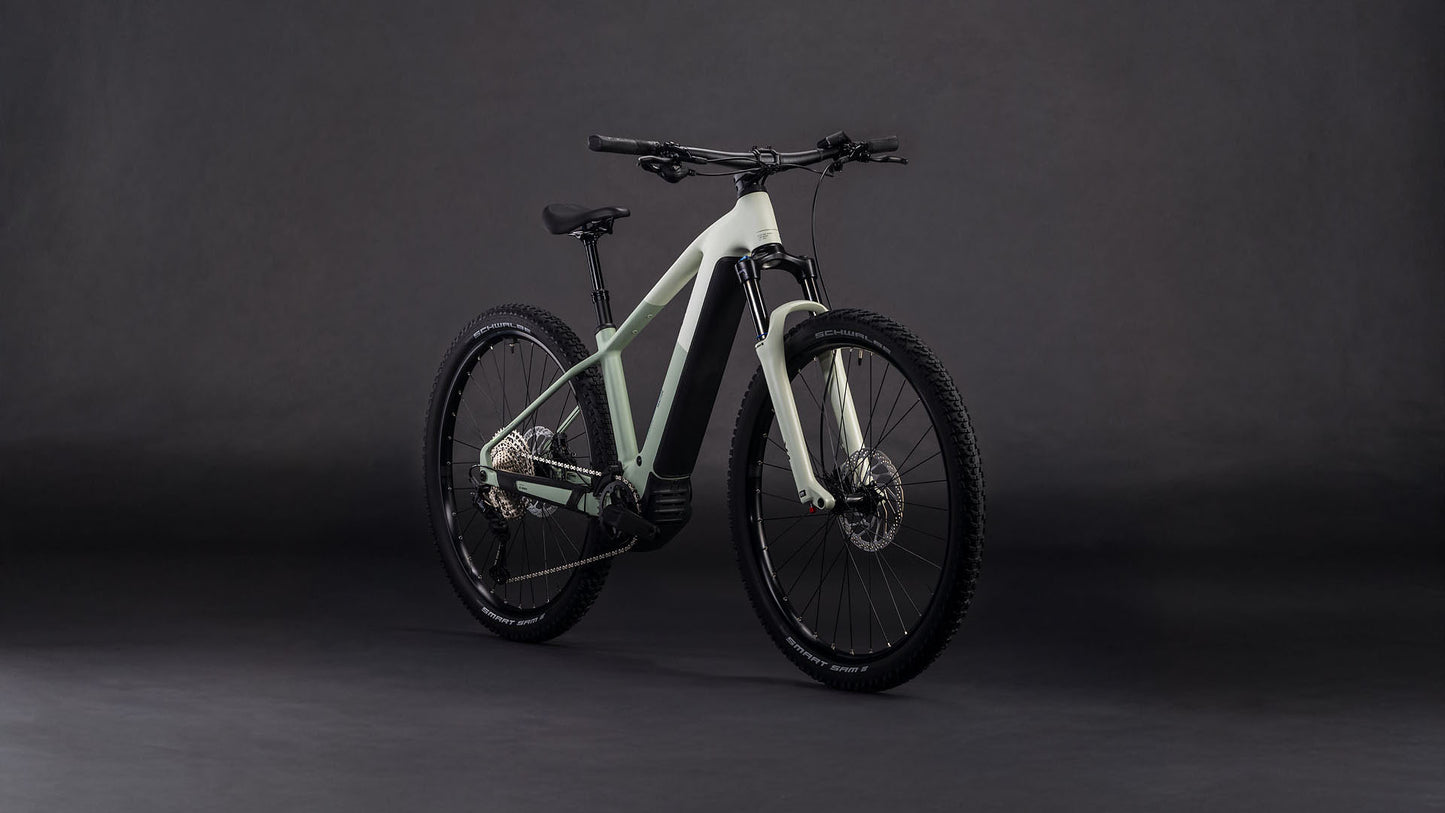 Das CUBE Reaction Hybrid Pro 800 desertstone'n'driedherbs 2026 E-Mountainbike mit hellem Rahmen, breiter Bereifung, 800-Wh-Akku und robustem Design wird vor einem dunklen, neutralen Hintergrund präsentiert.