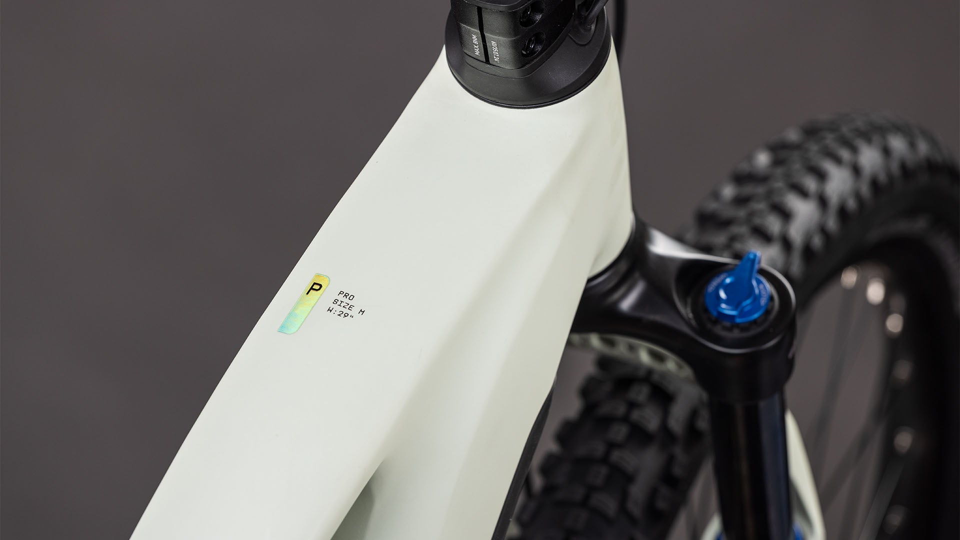 Nahaufnahme des CUBE Reaction Hybrid Pro 800 desertstone'n'driedherbs Trapeze 2026 Rahmens, mit Hervorhebung des Oberrohrs, der Federgabel und eines Aufklebers mit Text und einer Grafik; der Hintergrund ist unscharf.