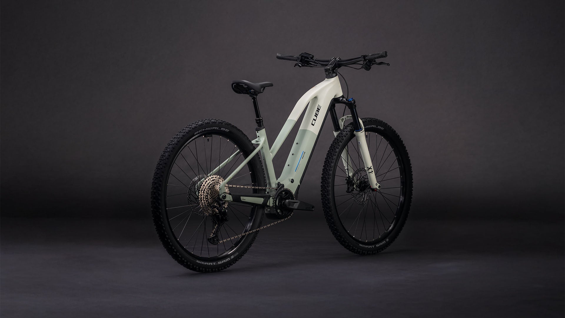 Das CUBE Reaction Hybrid Pro 800 desertstone'n'driedherbs Trapeze 2026 ist ein modernes E-Mountainbike mit dicken Reifen, integriertem 800-Wh-Akku und Vorderradfederung, abgebildet auf einem Hintergrund mit dunklem Farbverlauf.
