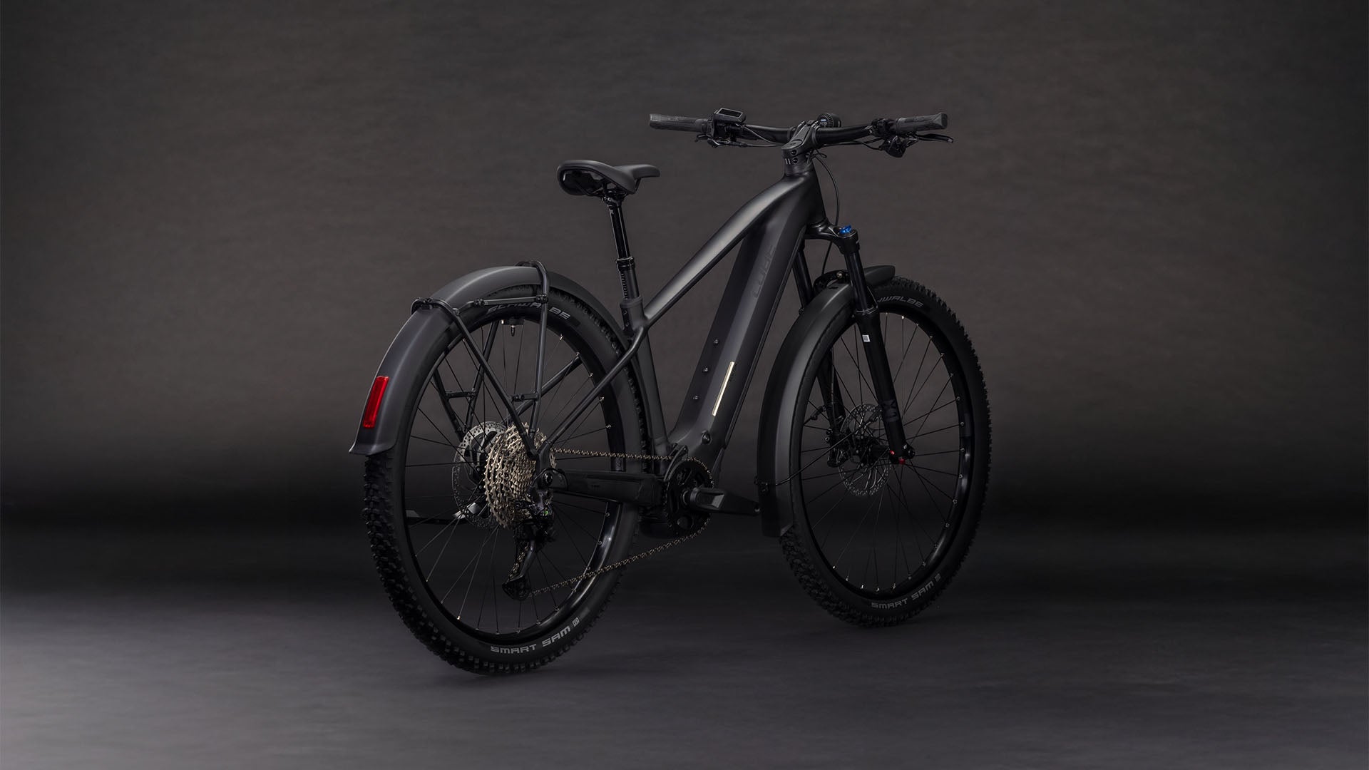 Das CUBE Reaction Hybrid Pro 800 FE blackline 2026 E-Mountainbike verfügt über dicke Reifen, Scheibenbremsen, einen eingebauten Akku, Schutzbleche vorne und hinten, ein sportlich-modernes Design und einen leistungsstarken Bosch CX-Motor - und das alles vor einem dunklen Hintergrund.