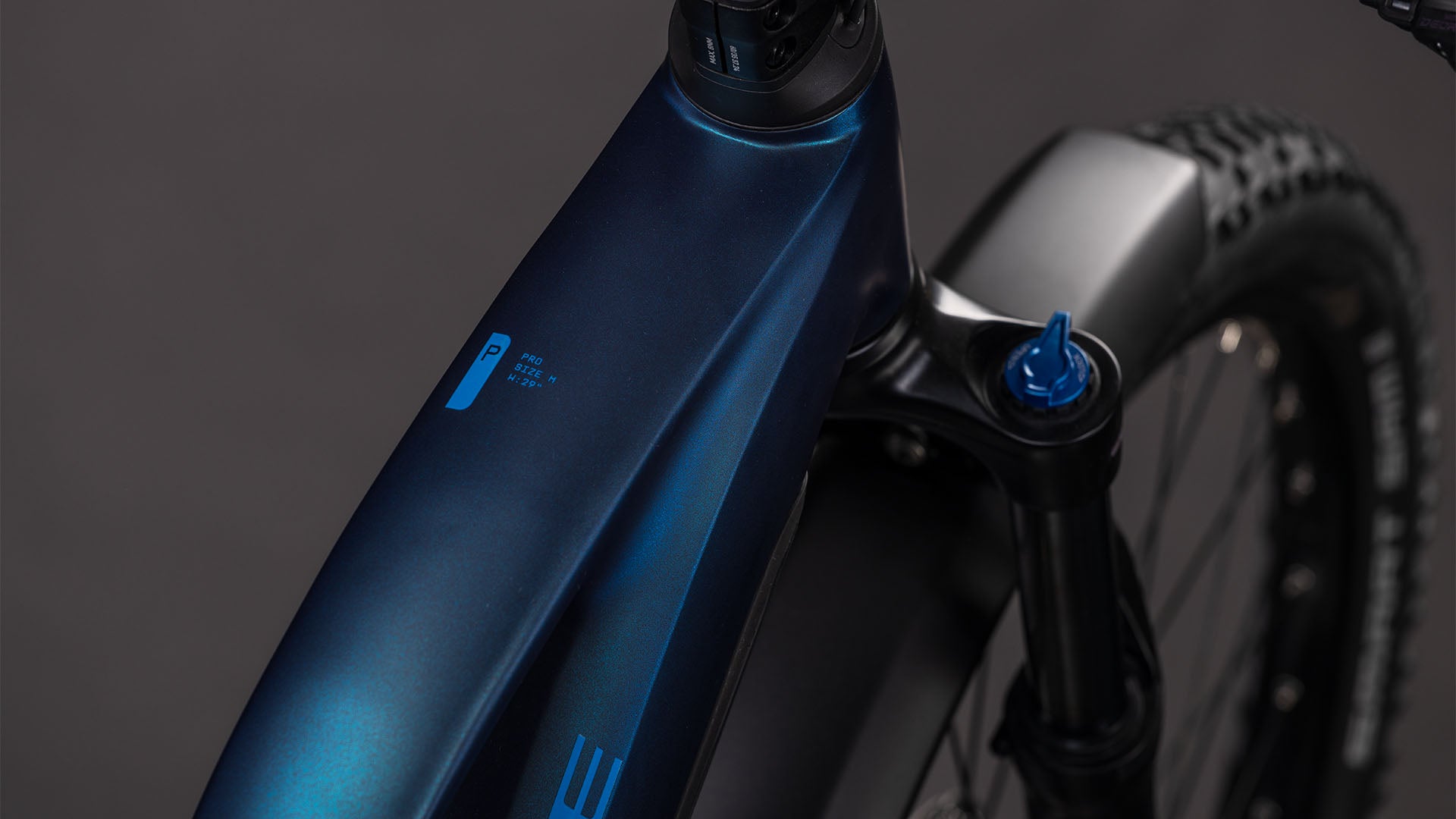 Nahaufnahme des dunkelblauen CUBE Reaction Hybrid Pro 800 FE nebular'n'dazzle Trapeze 2026 Rahmens mit Federgabel, Reifen und Batterieanzeige. Der Bosch CX-Motor verspricht eine starke Leistung. Der Hintergrund ist dunkelgrau und unscharf.