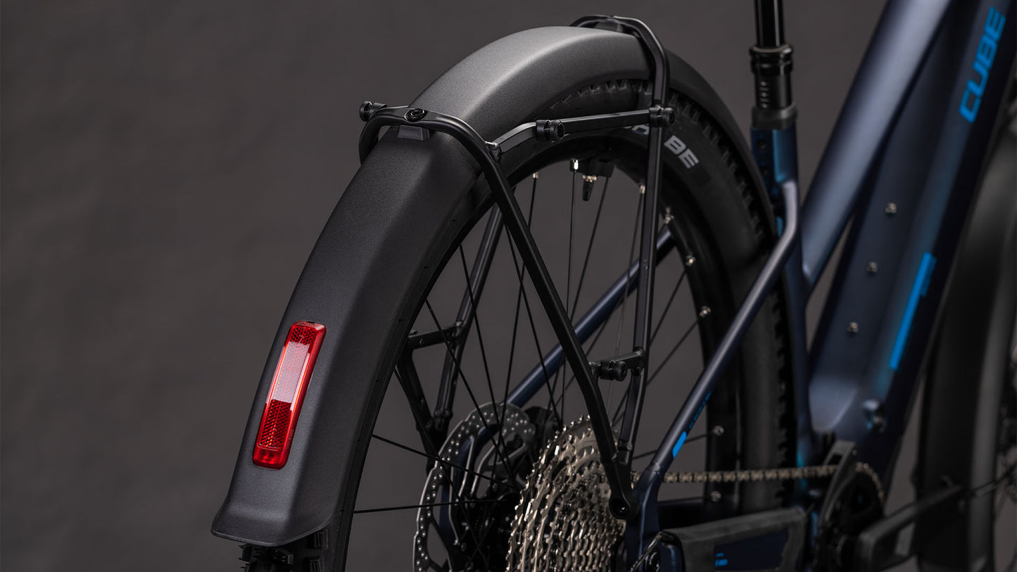 Nahaufnahme des Cube Reaction Hybrid Pro 800 FE nebular'n'dazzle Trapeze 2026 von CUBE, die das Hinterrad, das Schutzblech, den Bosch CX-Motor, den Antriebsstrang, die Shimano XT-Schaltung, den Reflektor und den Rahmen vor einem dunklen Hintergrund zeigt.