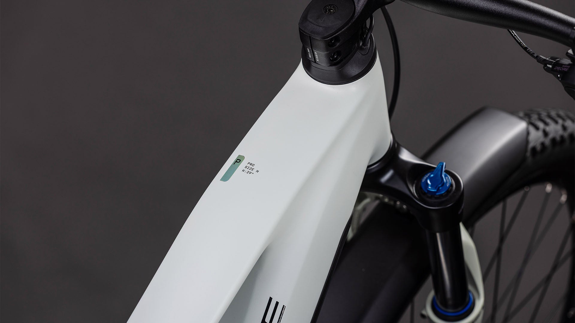 Nahaufnahme des Cube Reaction Hybrid Pro 800 FE desertstone'n'driedherbs 2026 von CUBE mit seinem modernen weißen Rahmen, der Digitalanzeige am Oberrohr, dem sichtbaren Lenker, der Federgabel und den strukturierten Reifen vor einem dunklen Hintergrund.