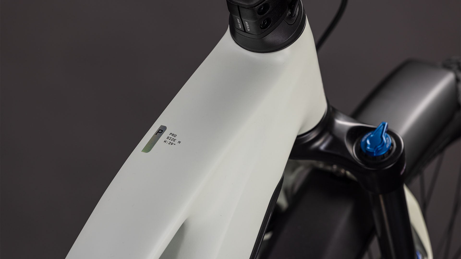 Nahaufnahme des CUBE Cube Reaction Hybrid Pro 800 FE desertstone'n'driedherbs Trapeze 2026 E-Bike-Rahmens in der Nähe des Lenkers, die eine kleine LED-Anzeige mit Akku- und Leistungsinformationen vor einem dunklen Hintergrund zeigt.