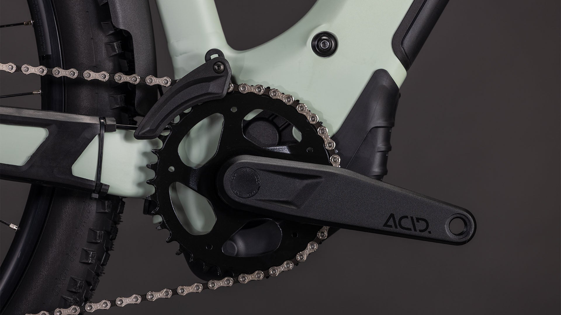 Nahaufnahme des CUBE Reaction Hybrid Pro 800 FE Trapeze 2026 in desertstone'n'driedherbs mit schwarzer ACID-Kurbelgarnitur, Kettenblatt und Kette. In den grün-schwarzen Rahmen sind ein Bosch CX Motor und eine Shimano XT 12-fach Schaltung integriert; der Hinterreifen ist teilweise zu sehen.