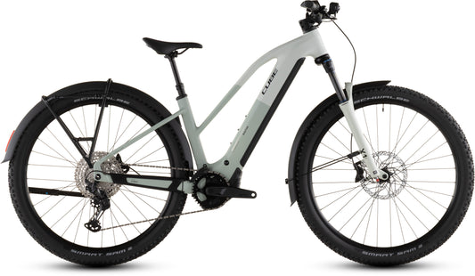 Das CUBE Reaction Hybrid Pro 800 FE desertstone'n'driedherbs Trapeze 2026 E-Bike verfügt über einen Bosch CX Motor, eine Shimano XT 12-fach Schaltung, einen schwarzen Sattel, breite Reifen, eine Vorderradfederung, Scheibenbremsen und Schutzbleche in einem modernen hellgrauen Profil.