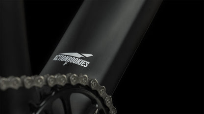 Nahaufnahme des mattschwarzen CUBE Elite 240 C:62 Pro carbon'n'blue'n'red 2024-Rahmens mit weißem CUBE-Logo in der Nähe der Fahrradkette und des Kettenblatts vor einem schwarzen Hintergrund.