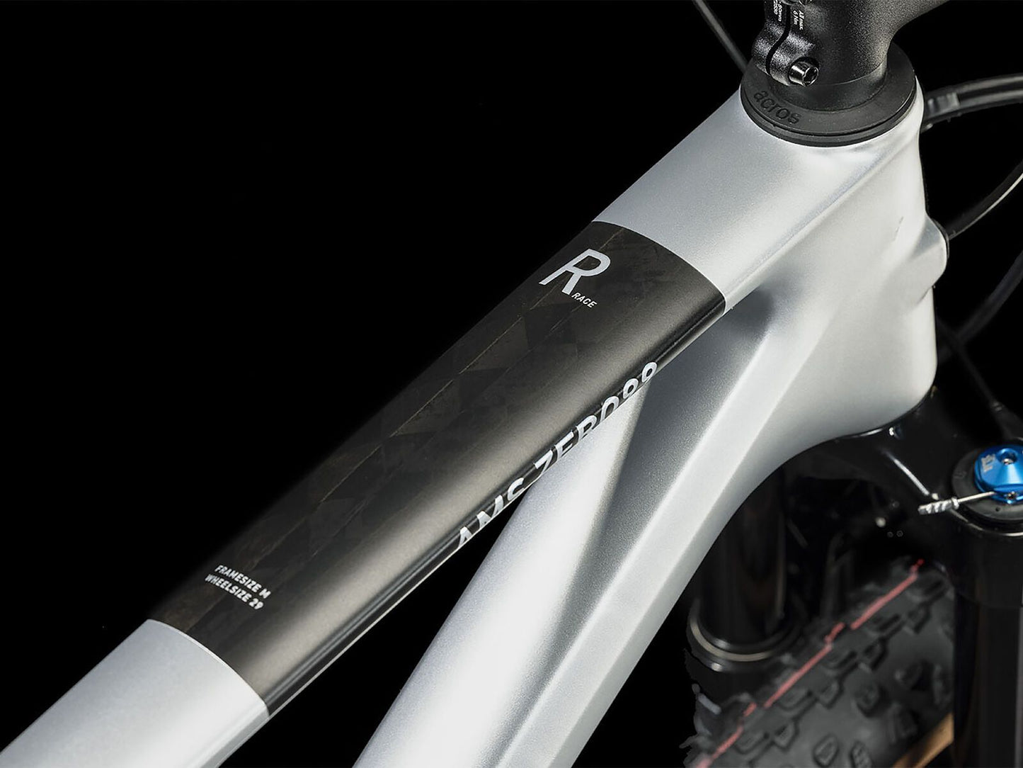 Nahaufnahme des Cube CUBE AMS ZERO99 C:68X Race 29 in silver'n'black, mit einem Carbonrahmen mit schwarzen geometrischen Details. Das Oberrohr zeigt ein "R"; ein Teil des Vorderrads und der Federgabel erscheinen vor einem schwarzen Hintergrund für maximale Effizienz.
