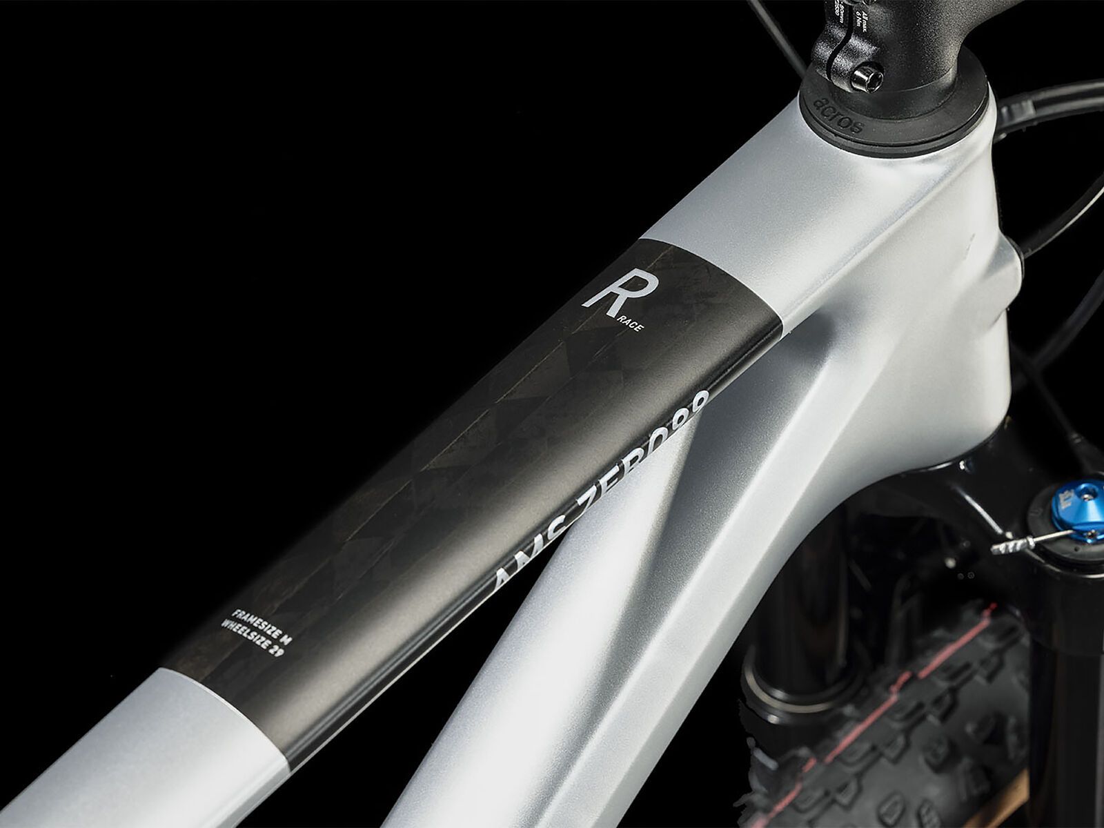 Nahaufnahme des Cube CUBE AMS ZERO99 C:68X Race 29 in silver'n'black, mit einem Carbonrahmen mit schwarzen geometrischen Details. Das Oberrohr zeigt ein "R"; ein Teil des Vorderrads und der Federgabel erscheinen vor einem schwarzen Hintergrund für maximale Effizienz.