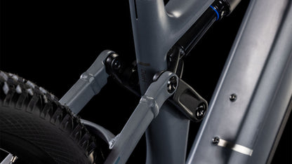 Nahaufnahme des CUBE Stereo Hybrid ONE77 HPC Race 800 Federungsgestänges in slapgrey'n'prism, die den Rahmen, den Stoßdämpfer und das Hinterrad zeigt, die durch glatte metallgraue Komponenten mit sichtbaren Schrauben vor einem schwarzen Hintergrund verbunden sind.
