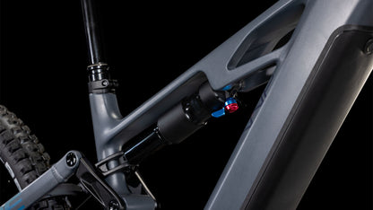 Nahaufnahme des CUBE Stereo Hybrid ONE77 HPC Race 800 slapgrey'n'prism 2025-Rahmens, mit Blick auf die Hinterradaufhängung und die blau-roten Einstellknöpfe für die Stoßdämpfer, vor schwarzem Hintergrund.