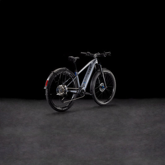 Das CUBE Reaction Hybrid Pro 800 Allroad metallicgrey'n'black 2025, ein modernes E-Bike mit dicken Reifen, Schutzblechen und hydraulischen Scheibenbremsen, wird von hinten links auf dunklem Hintergrund gezeigt.
