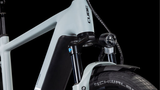 Nahaufnahme des Vorderrahmens, der Gabel, der Federung, des Schwalbe-Reifens, des Bosch CX-Motors und des Scheinwerfers des CUBE Kathmandu Hybrid EX 800 haze´n´black 2025. Markendetails und elegante Designelemente heben sich vom schwarzen Hintergrund ab.
