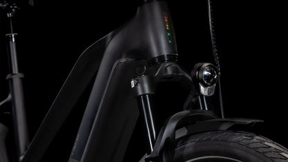 Die Nahaufnahme des CUBE Kathmandu Hybrid EXC 800 black'n'prism Trapeze 2025 zeigt die mattschwarze Front mit Federgabel, Scheinwerfer und einem Teil des Vorderreifens vor einem schwarzen Hintergrund.