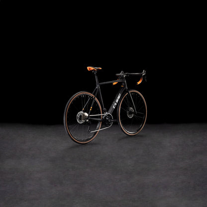 Das CUBE Cross Race C:62 Pro carbon'n'orange 2025 Rennrad mit Carbonrahmen und auffälligen orangefarbenen Akzenten wird vor einem dunklen Hintergrund präsentiert, um sein modernes, aerodynamisches Design zu unterstreichen.