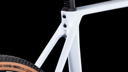 Nahaufnahme des CUBE Cube Cross Race C:62 Race polarwhite'n'blue 2025 Rahmens. Hervorzuheben sind der Sitzrohrübergang, die Sitzstreben und das Hinterrad mit hellbraunen Seitenwänden vor einem schwarzen Hintergrund.