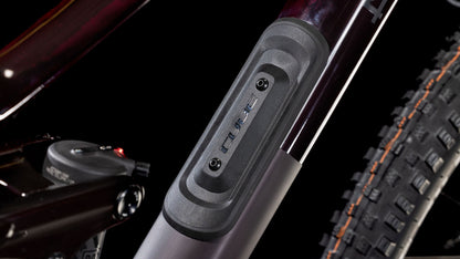 Nahaufnahme des CUBE Stereo ONE44 C:68X SLX 29 liquidviolet'n'black 2025 Carbon-Rahmens, die eine rechteckige "CUBE"-Anschlussabdeckung mit zwei Schrauben in der Nähe des Hinterrads und der Aufhängung zeigt, vor einem schwarzen Hintergrund.
