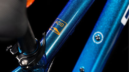 Nahaufnahme des metallic-blauen CUBE Acid 200 Disc Actionteam 2025 Mountainbike-Rahmens mit Sattelstützenklemme und orangefarbenem ACID-Label mit Berggrafik auf dem Oberrohr vor schwarzem Hintergrund.