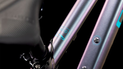 Nahaufnahme des CUBE Acid 200 Disc galactic´n´cyan 2025-Rahmens mit schillerndem lila-blauem Finish, teilweisem Logo, sichtbaren Schrauben und Sattelstütze sowie Details der Shimano 7-fach-Schaltung vor schwarzem Hintergrund.