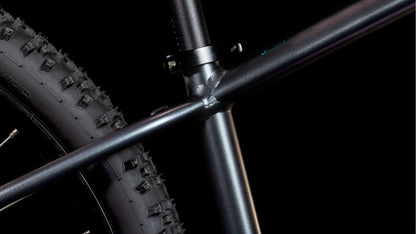 Nahaufnahme des hinteren Dreiecksgelenks und des Off-Road-Reifens des CUBE Acid 260 Disc galactic'n'cyan 2025 vor einem schwarzen Hintergrund - ideal für jeden Mountainbiker. Marke: CUBE.
