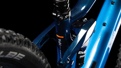 Nahaufnahme des Cube Stereo ONE22 Rookie actionteam Rahmens von CUBE mit Hinterradfederung, HPA-Label, Teil eines dicken Schwalbe-Reifens und Shimano 11-fach Schaltung auf schwarzem Hintergrund.
