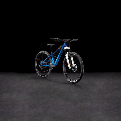 Das Cube Stereo ONE22 Rookie actionteam von CUBE, mit dicken Reifen und einer Shimano 11-fach Schaltung, ist in blau und weiß auf einem schlichten dunklen Hintergrund abgebildet, leicht nach links geneigt.