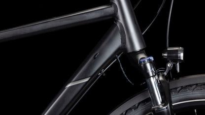 Nahaufnahme des CUBE Nature ONE Allroad black'n'black Rahmens und der Federgabel, mit einem Teil des Vorderrads und einem Scheinwerfer vor einem schwarzen Hintergrund.
