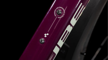 Nahaufnahme des lilafarbenen Rahmens eines CUBE Nature ONE Allroad amarone'n'lunar 2025 mit einer Schraube und dem Schriftzug "DESIGNED AND ENGINEERED IN GERMANY", einem Teil des CUBE-Logos, sowie Shimano 1x8-Gang-Schaltungskomponenten.