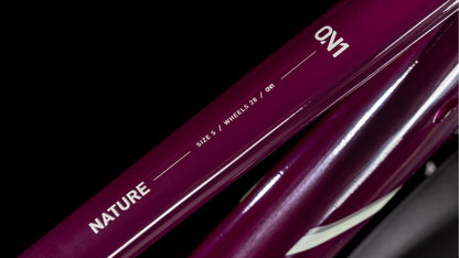 Nahaufnahme des Cube Nature ONE Allroad amarone'n'lunar Trapeze 2025, mit den Schriftzügen "NATURE", "SIZE 5", "WHEELS 28" und "ON1" auf einem lilafarbenen Rahmen, mit Shimano 1x8-Gang Schaltung, vor schwarzem Hintergrund. Marke: CUBE.