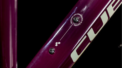 Nahaufnahme des CUBE Nature ONE Allroad amarone'n'lunar Trapeze 2025 Trekkingrad-Rahmens mit einer Schraube, einem Schild mit der Aufschrift DESIGNED AND ENGINEERED IN GERMANY, einem Teil des CUBE-Logos und Details der Shimano 1x8-Gang Schaltung.