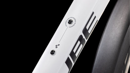 Nahaufnahme eines Cube Nature Pro Allroad cotton'n'grey 2025 Rahmens von CUBE, mit zwei Schraubenhaltern und "DESIGNED AND ENGINEERED IN GERMANY" daneben. Auf dem weißen Aluminiumrahmen sind fette "UBE" und teilweise Shimano Cues Schaltung zu sehen.