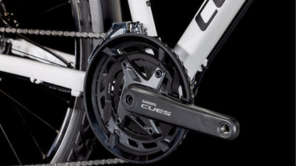 Nahaufnahme einer Shimano CUES-Kurbelgarnitur und Kette mit dem Logo auf dem Kurbelarm, montiert auf einem CUBE Nature Pro Allroad cotton'n'grey 2025 Aluminiumrahmen mit schwarzem Hintergrund.